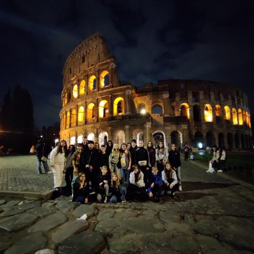 Gruppenfoto vor dem beleuchteten Kolosseum am Abend. 